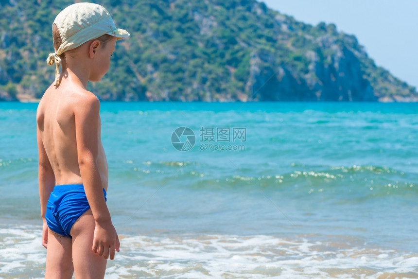 5岁的男孩在泳裤里看着海浪图片
