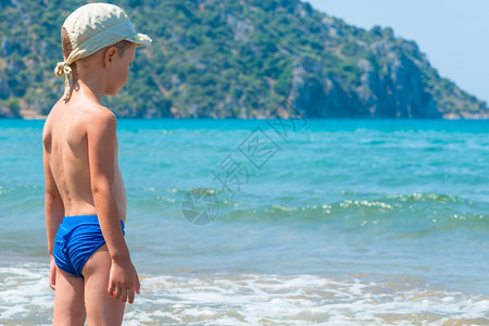 5岁的男孩在泳裤里看着海浪图片