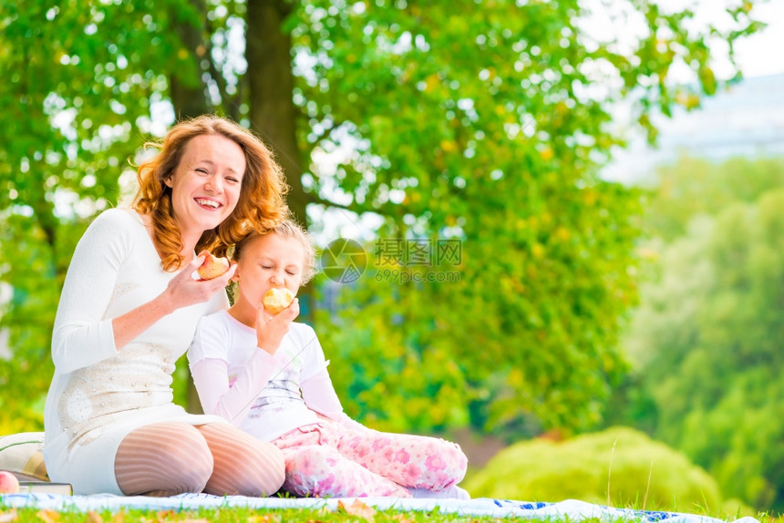 年轻母亲和女儿在公园吃苹果图片
