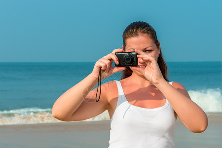 女人用照相机在海滩拍照图片