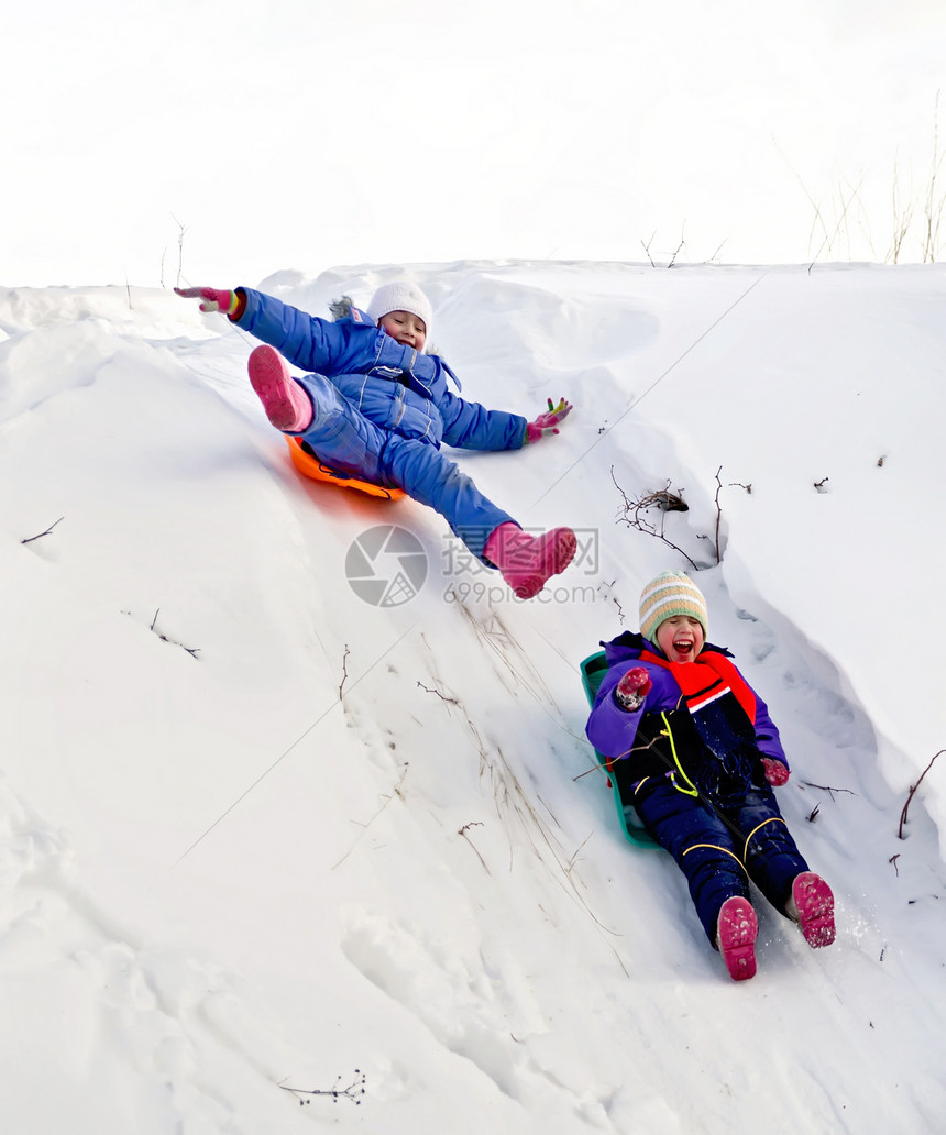 两个小女孩在雪橇上滑下山坡在冬天雪图片