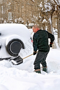 一个男人在挖被雪覆盖的汽车图片