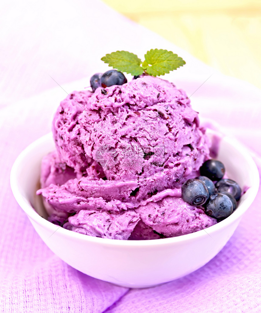 蓝莓冰淇淋夹薄荷和浆果碗里有在木板背景上的紫色餐巾纸上图片