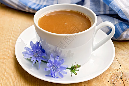 在一个白杯中饮用花朵木板背景上的蓝布图片