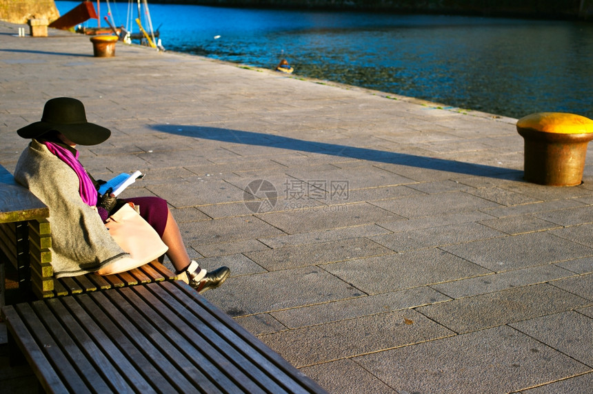 波尔图河堤岸的长椅上妇女阅读一本书图片