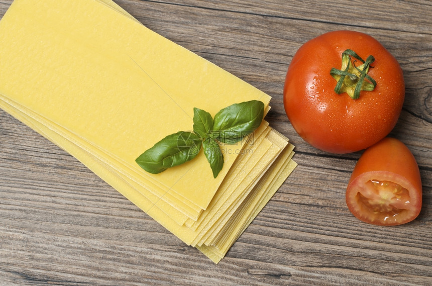 鲜意大利面条配有叶和木本背景的新鲜番茄图片