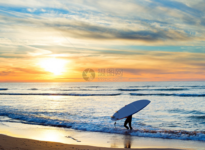 日落时在海滩上携带冲浪板的男子图片