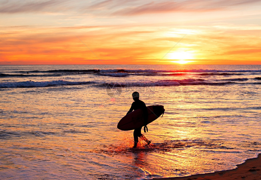 日落时沙滩上有冲浪板的者背影图片