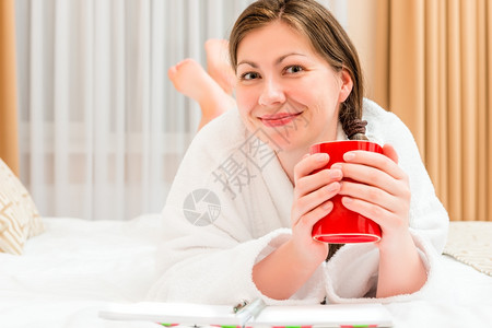 穿着浴袍的女孩在床上喝茶图片