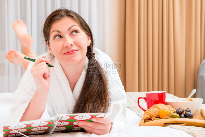 年轻女子在床上写笔记本吃早餐图片