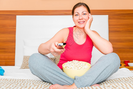 年轻女性拿着爆米花坐在床上看电视图片