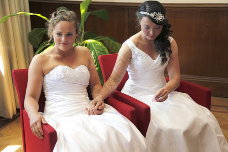 两位结婚的新娘手握着双坐在红椅子上图片