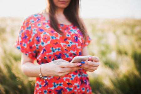 迷人的年轻女使用移动智能手机对抗夏天的绿色图片