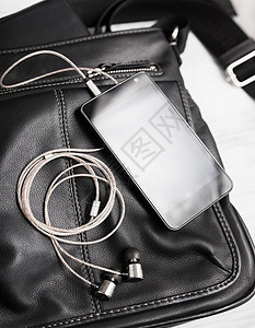 用耳机在黑皮包上装有耳机的智能手图片