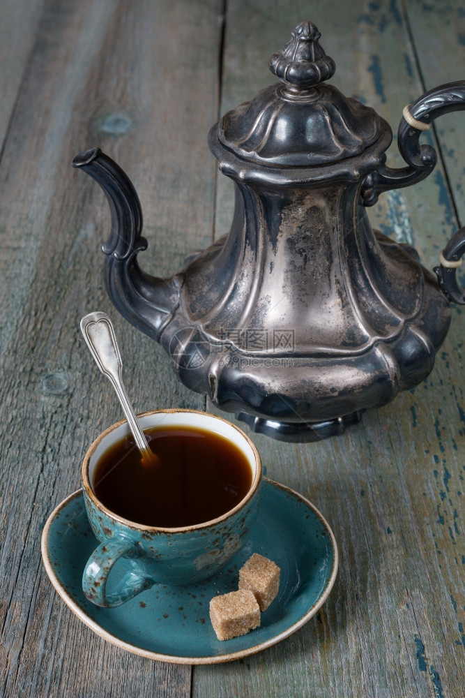 蓝色旧咖啡杯中的黑和旧木板上的古董银咖啡壶图片