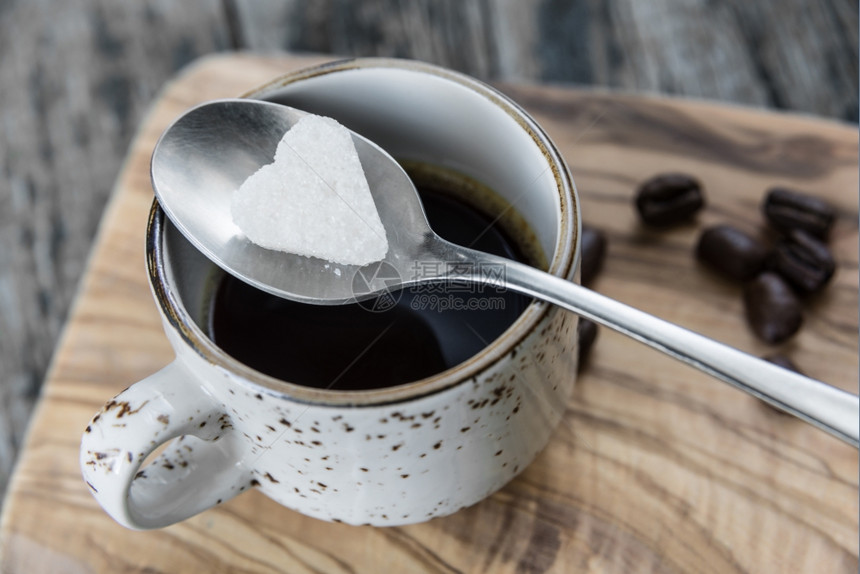 一小块白糖以心脏的形式躺在茶匙上一杯黑咖啡上图片