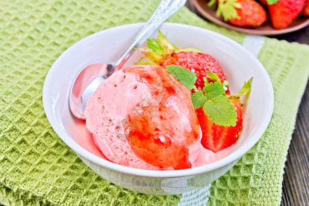 白碗中的草莓糖浆和在木板背景上的绿餐巾纸勺子草莓冰淇淋图片