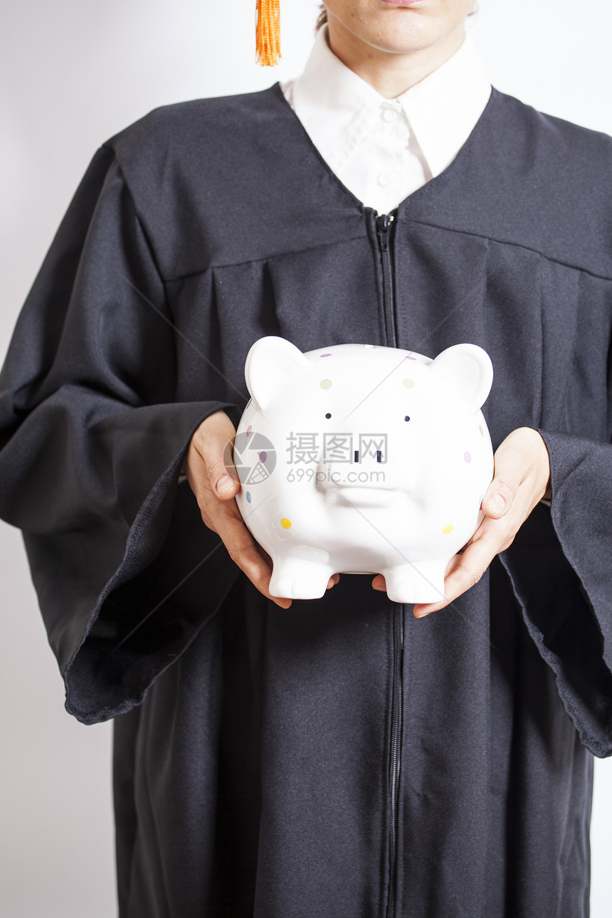 毕业生穿戴帽子和礼服持有小猪存钱罐图片