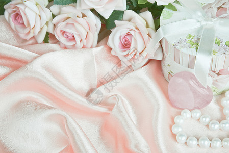 粉红玫瑰圆礼盒和丝织物上的珍珠项链图片