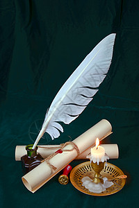 羽毛灯墨水井的白色羽毛燃烧蜡烛和两卷纸在深绿布上背景