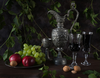 马口铁仍然生活在中世纪的方式中古老的投手和满红酒以及胡桃绿葡萄和含色植物的黑暗背景古老酒瓶和满了红葡萄酒和胡桃绿葡萄内水龙头的酒杯中充背景