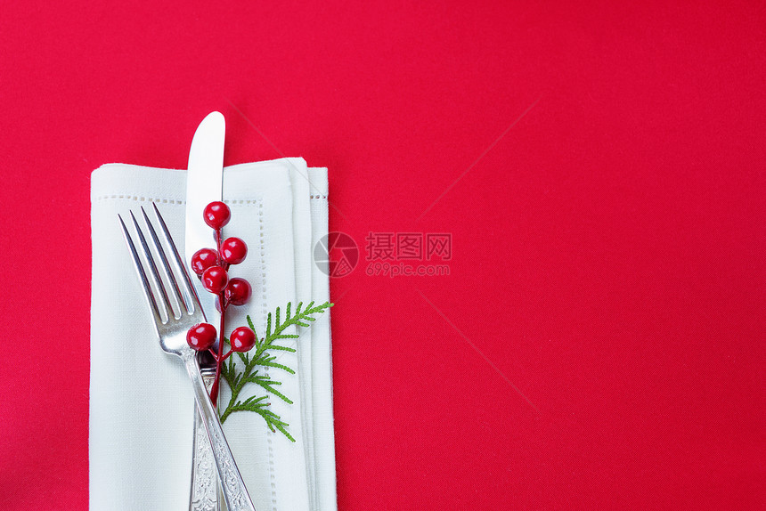 白纸巾上有红色胡利浆果和绿瓜树枝白纸巾放在一张桌子上面有一张红色桌布上面是一张红色桌布图片