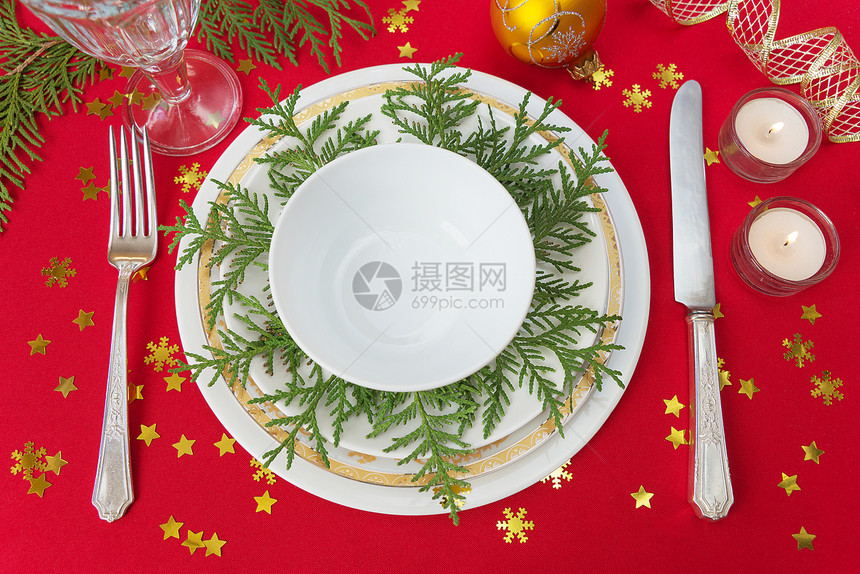 银刀叉餐盘葡萄酒杯和燃烧的蜡烛放在一张桌子上面有一张红桌布上面有雪花形的金条图片