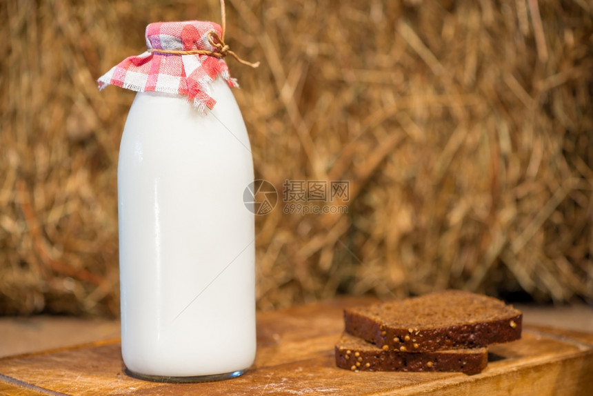 瓶装牛奶和一块黑麦面包在稻草背景上图片
