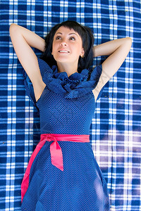 格子连衣裙穿着裙子的漂亮女孩躺在蓝色的格子上背景