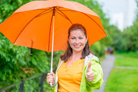 满意的女人在公园散步时拿着雨伞图片