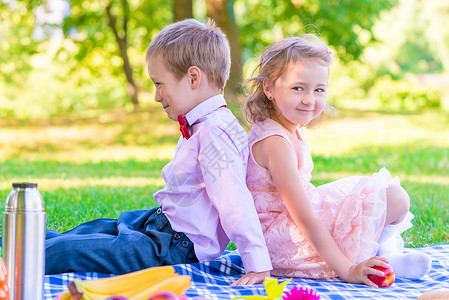 6岁男孩和女孩在野餐中背对背相坐图片