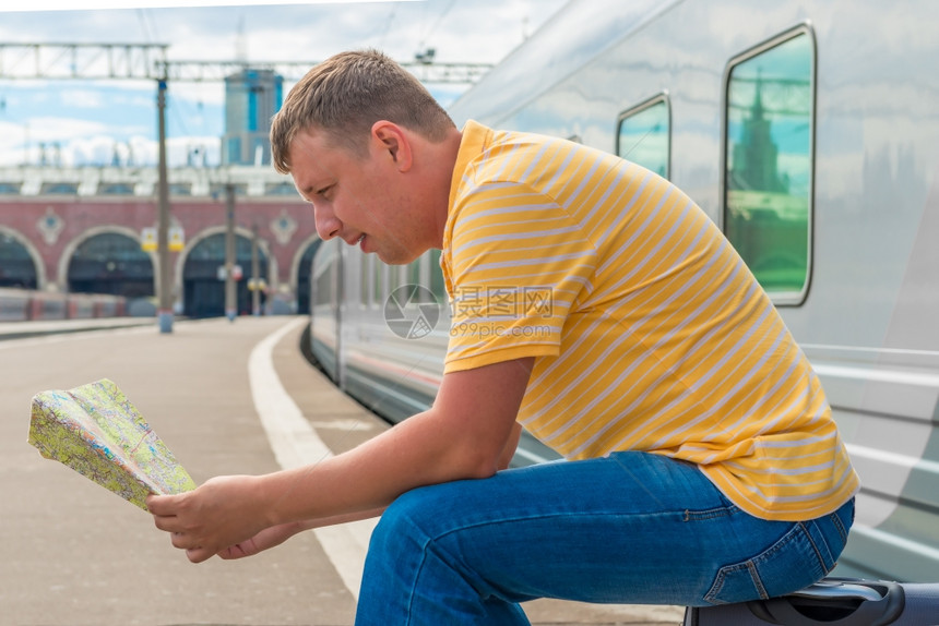 男子坐在火车站的手提箱上正在研究图片
