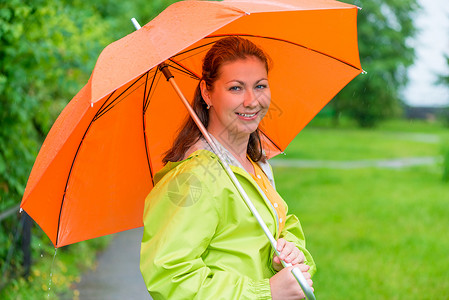 拿着雨伞的女孩30岁的笑女孩拿着雨下的伞背景