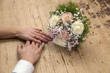 美甲结婚素材新娘和郎的手结婚戒指在木桌上玫瑰花束背景