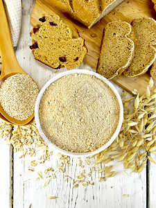 无白梭子鱼面粉在白碗中燕麦面在勺子中燕麦和茎面包饼干在顶木板上的背景背景