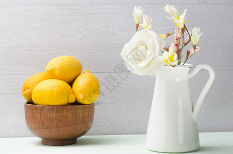 玫瑰柠檬茶壶里装着柠檬和白花的木碗背景