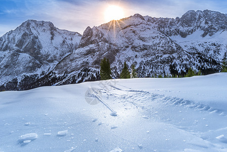 雪山和牧场上的冰壳冬季明亮的一天高山风景冰壳上的细节位于奥斯特里亚山的牧场表面由于太阳的温暖从岩石峰后面发光背景图片