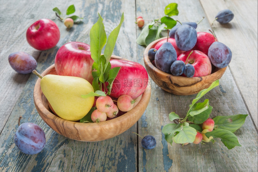 几个红苹果绿色叶子蓝李和梨在旧木桌的碗里图片