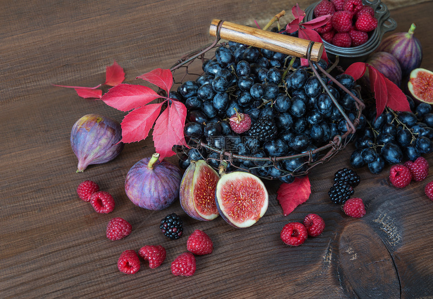 篮子中的黑葡萄和成熟无花果红草莓和木本底有秋叶的黑莓图片