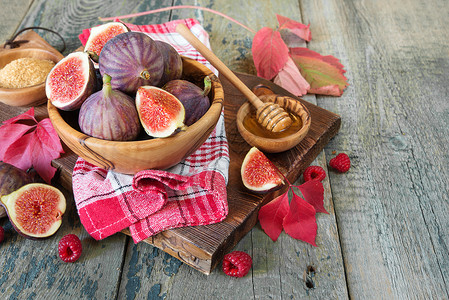 作文木制的木碗红草莓甘蔗糖蜂蜜中的成熟无花果旧切割板上的餐巾纸和秋叶都躺在旧木桌上背景