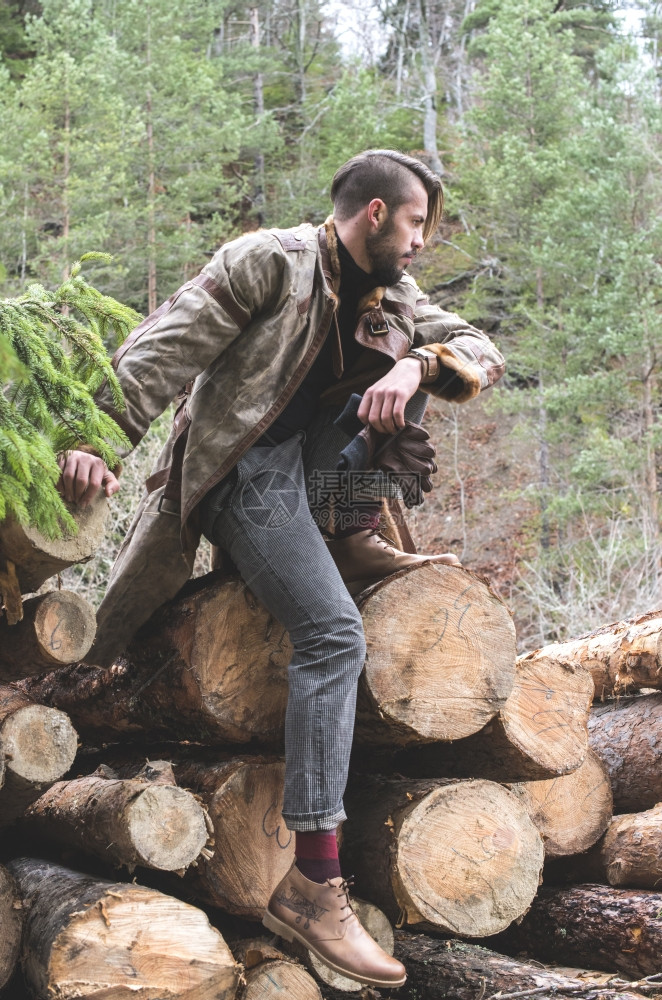 青年男子在森林的原木上展示皮革和牛仔裤户外时装图片