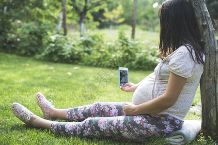 花园里使用智能手机的孕妇图片