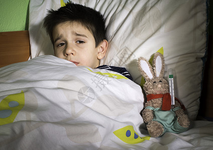 生病的孩子和泰迪熊躺在床上用温度计测量背景图片