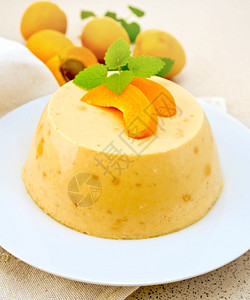 甜点椰子芝士蛋糕白盘里有杏子餐巾纸上的薄荷棕花岗岩桌背景上的水果图片