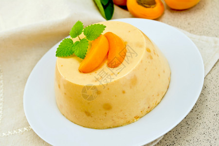 甜点pancot芝士蛋糕和白盘中的杏子餐巾上薄荷花岗岩桌上的水果图片