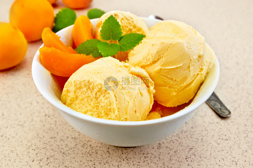 白碗中的杏仁冰淇淋里面有水果和薄荷片一勺子放在本底花岗岩桌上图片