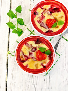 布丁草莓两碗加浆果和薄荷餐巾纸上布丁草莓背木板的景图片