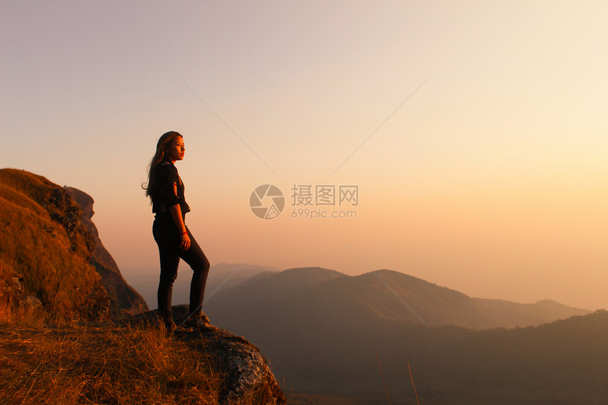 带着背包的年轻女孩在雾山峰享受日落旅游者在背景观赏模型上旅行远足者在泰国旅行时仰望阳光模拟文字图片