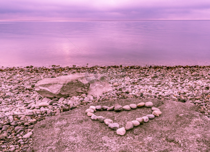 心形由石块制成放在大岩上湖边的预兆之下蓝棕色的天空下水中反射出来图片