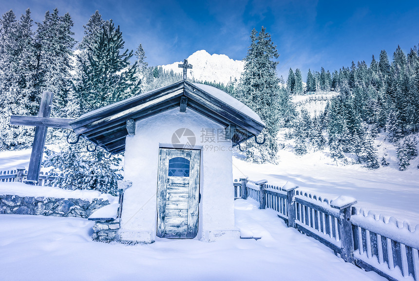 冬天的风景中高山的古老小教堂环绕着一座老木栅栏森林和山峰雪覆盖着图片